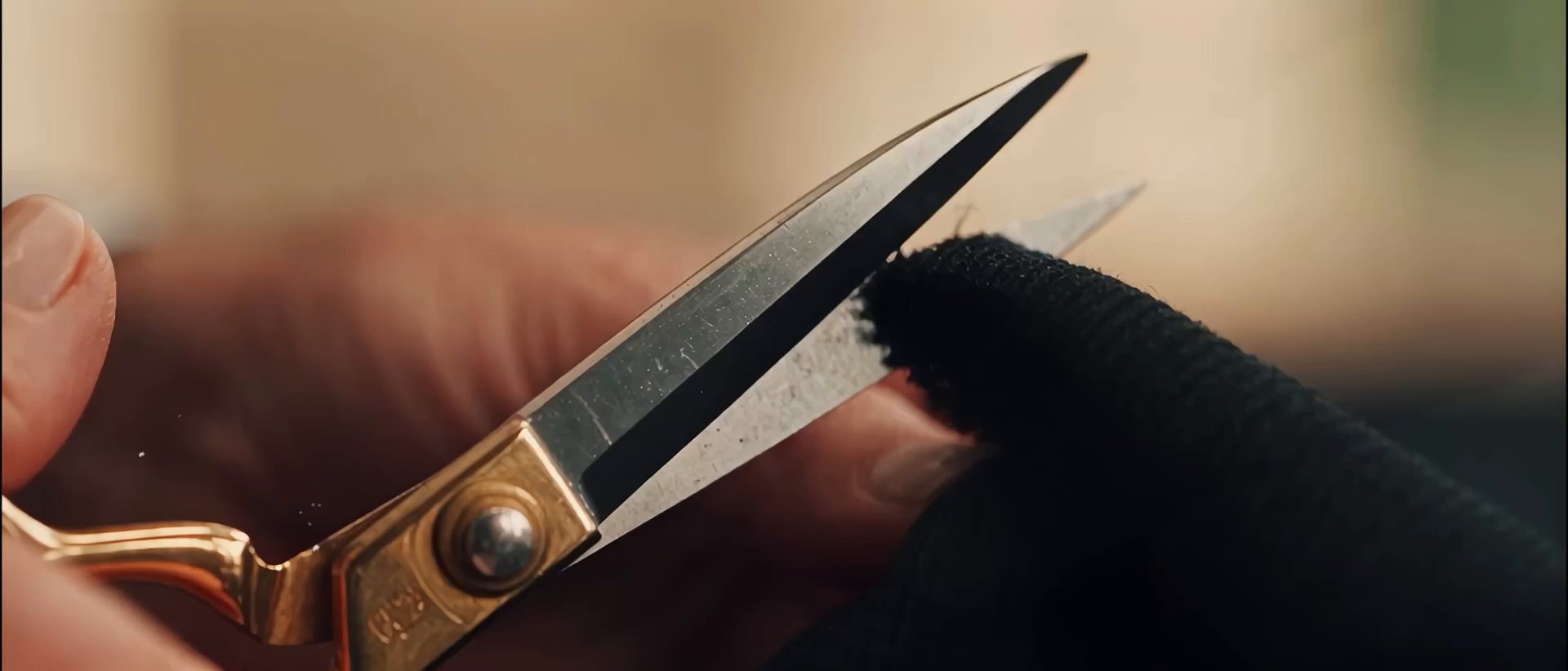 Brass-handled scissors cutting through black cloth.
