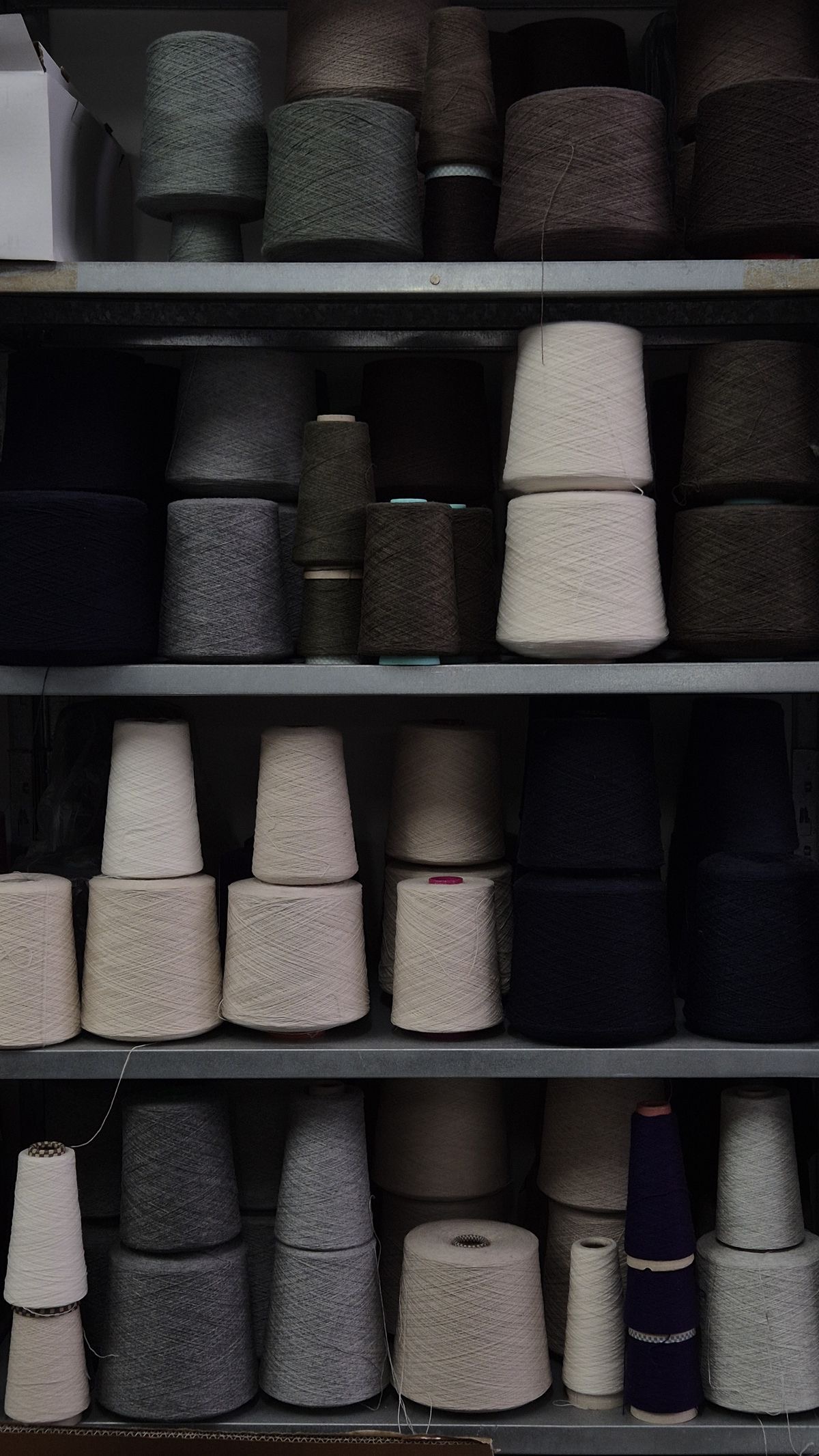 Cones of yarn in cream, grey and navy on workshop shelves.